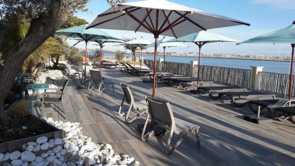 a row of tables and chairs with umbrellas and the water at Hôtel Les Brises in La Rochelle