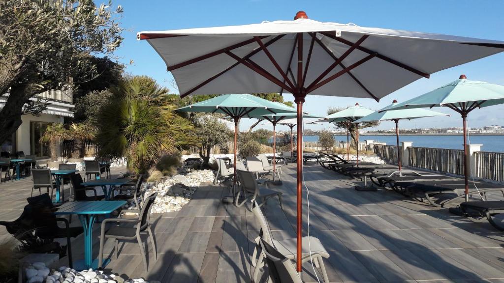 a group of tables and chairs with umbrellas on a beach at Hôtel Les Brises in La Rochelle