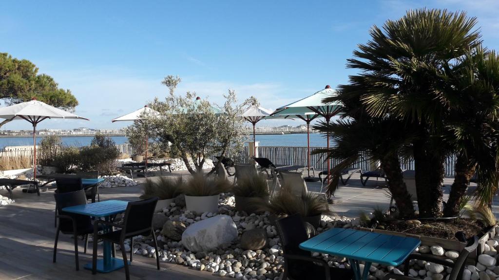 a patio with tables and chairs and palm trees at Hôtel Les Brises in La Rochelle