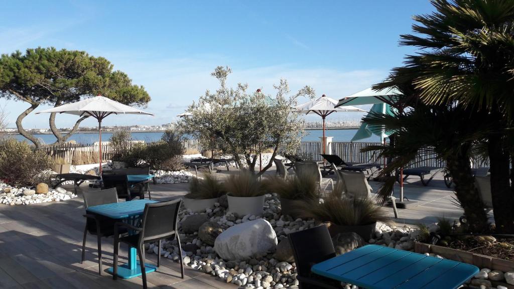 a patio with chairs tables and umbrellas on the beach at Hôtel Les Brises in La Rochelle