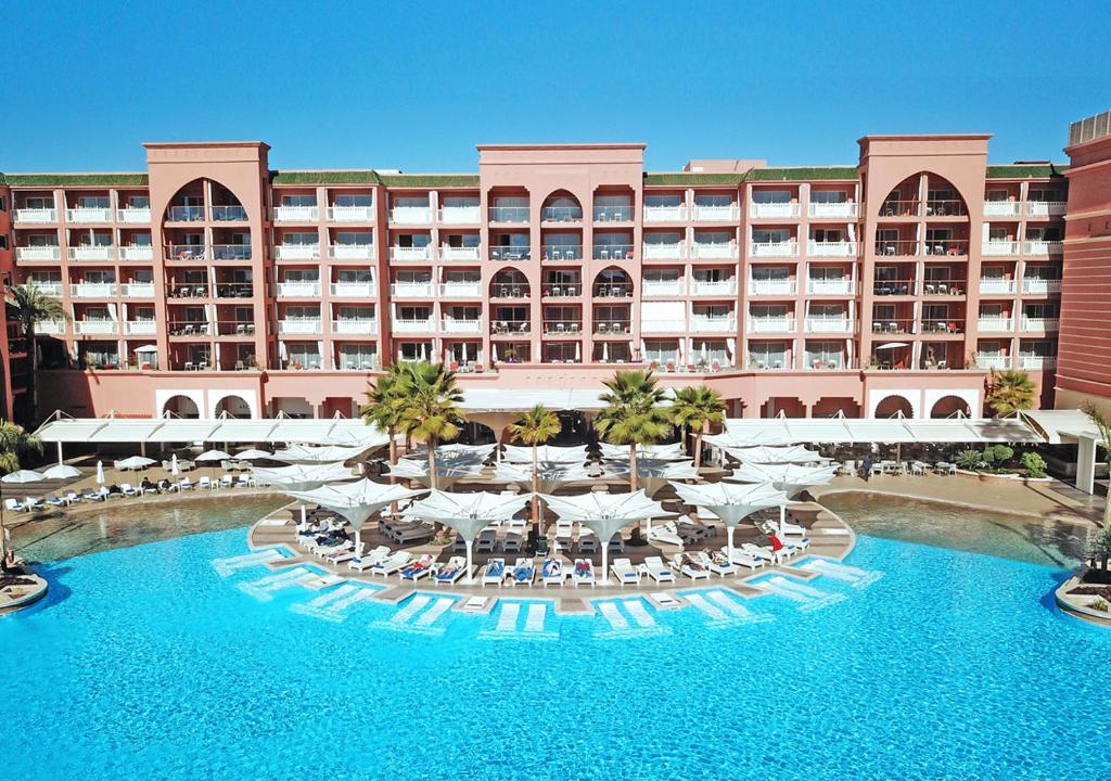 a hotel with a large pool with chairs and umbrellas at Savoy Le Grand Hotel Marrakech in Marrakesh