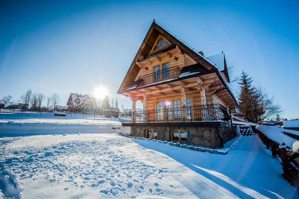 een blokhut in de sneeuw met de zon erachter bij Domek Góralski in Poronin