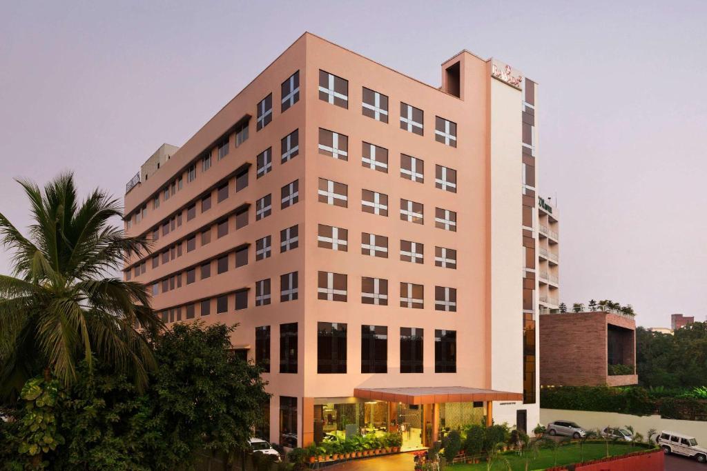 a tall pink building with a palm tree in front of it at Ramada Jamshedpur Bistupur in Jamshedpur
