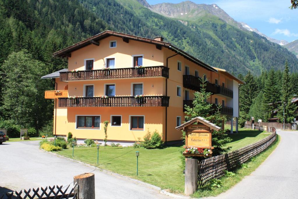 a large yellow house with a fence in front of a mountain at Hotel Hubertus in Mallnitz