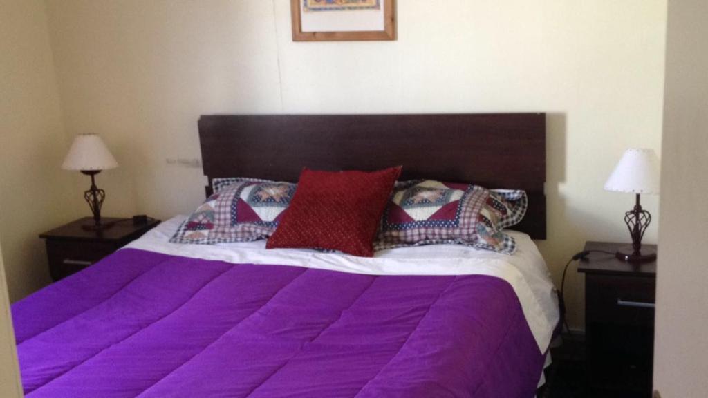 a bed with purple sheets and pillows on it at Cabaña la villa in Frutillar