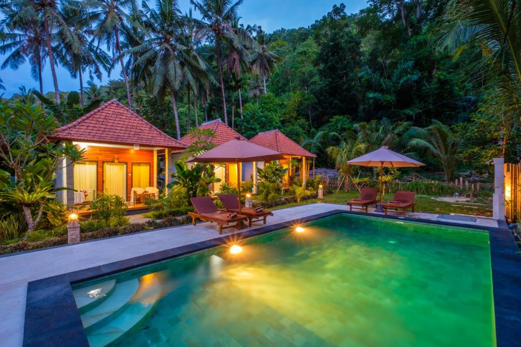 a pool with chairs and umbrellas in front of a house at Crystal Bay Bungalows in Nusa Penida