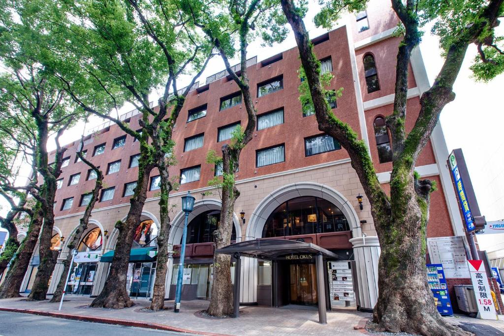 un gran edificio de ladrillo con árboles delante de él en Hotel Okus en Kumamoto