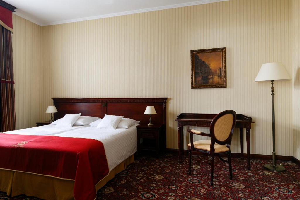 spacious hotel bedroom with large bed, red throw, writing desk, chair, and classic lamps