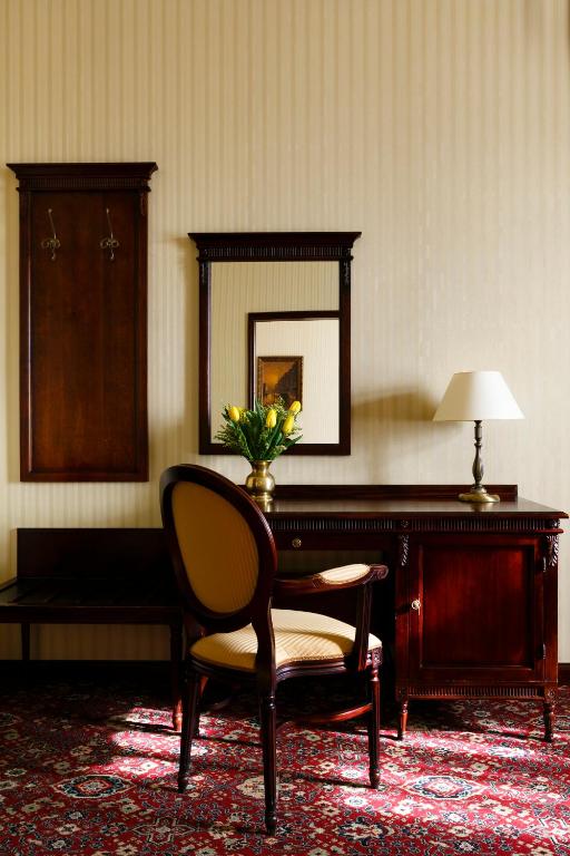 classic wooden desk and upholstered chair with mirror, lamp, and vase of yellow tulips