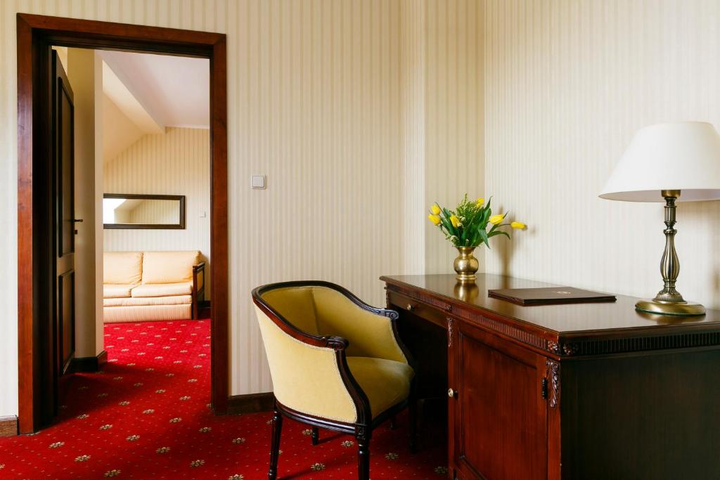 Elegant hotel sitting area with wooden desk, yellow armchair, vase of tulips, doorway to sofa