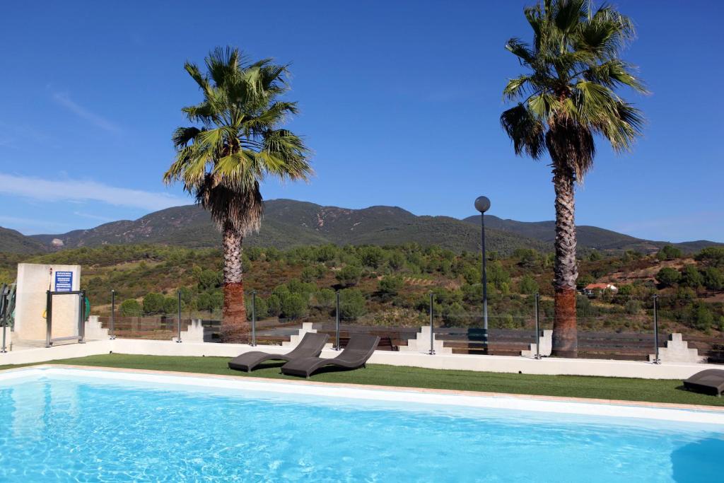 a swimming pool with chairs and palm trees and mountains at Logis Hôtel LE PRESSOIR in Saint-Chinian