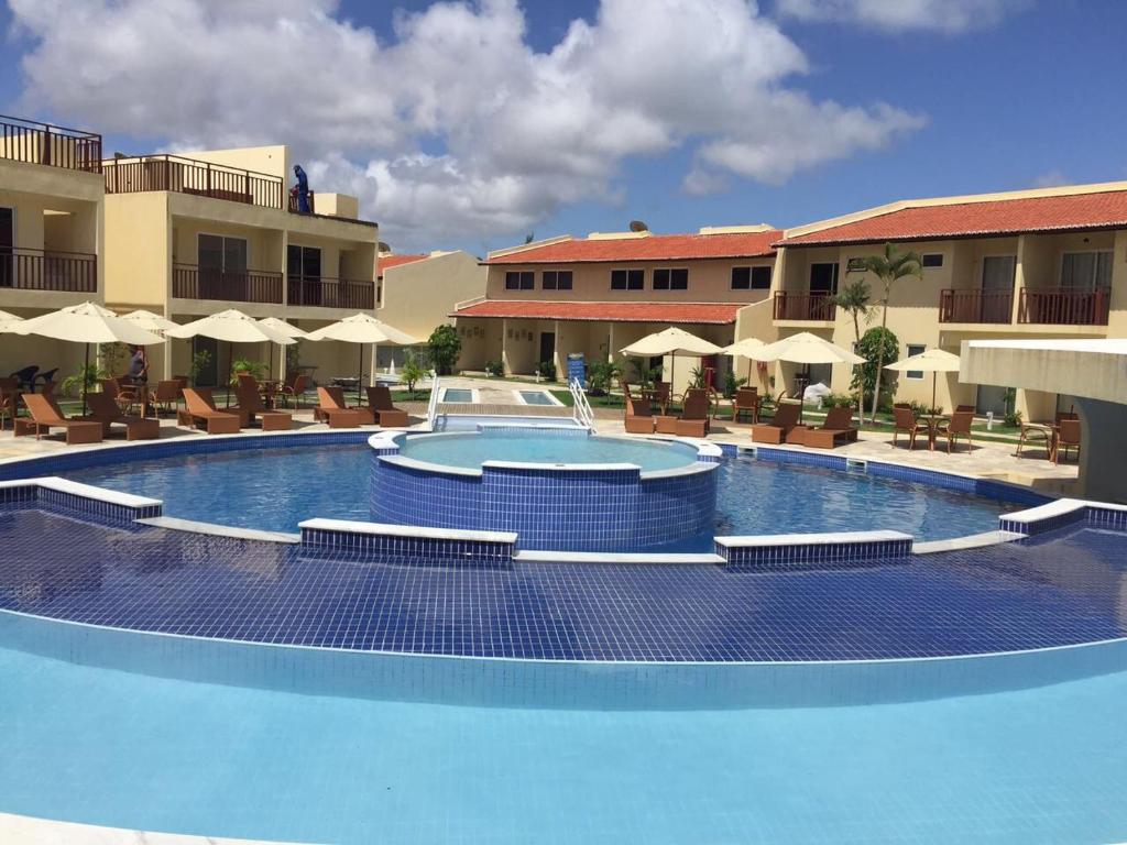 a large swimming pool in a resort with chairs and umbrellas at Solar Água - Apto. 114 in Pipa