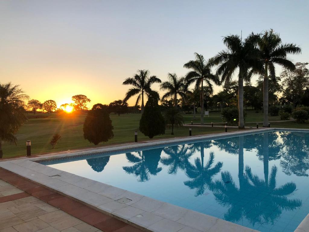 a pool with palm trees and the sunset in the background at Carlos Franco Country Golf in Arroyos y Esteros