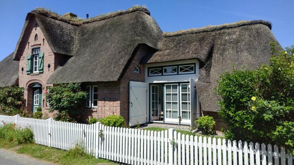 a thatch roof house with a white fence at Das Rosenhaus in Utersum