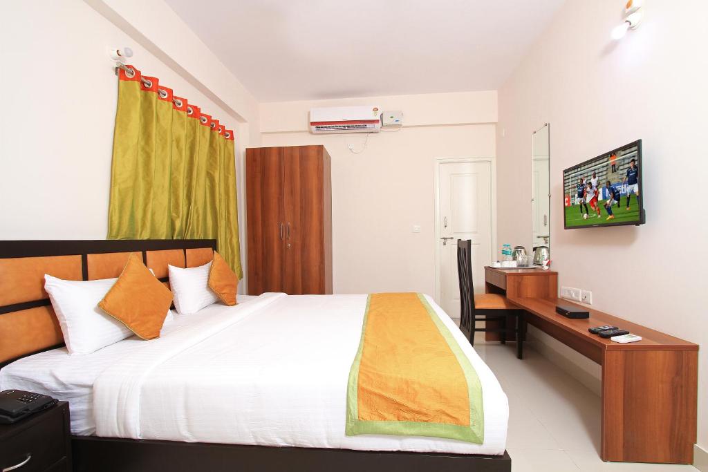 Schlafzimmer mit einem Bett, einem Schreibtisch und einem TV in der Unterkunft Arra Suites kempegowda Airport Hotel in Devanhalli