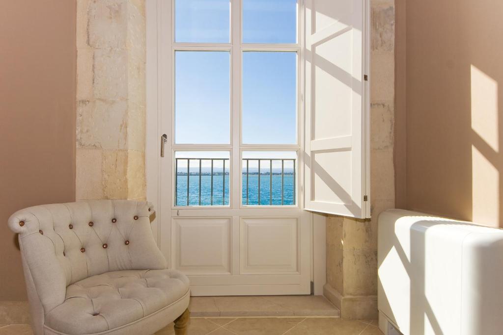 een witte stoel in een kamer met een raam bij Palazzo Alfeo Aparthotel in Siracusa