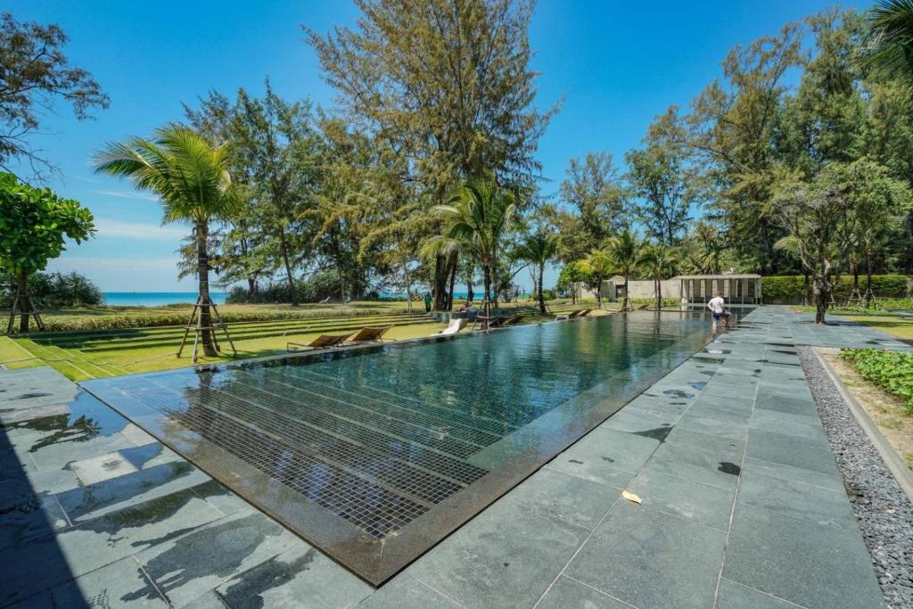 a swimming pool in the middle of a park with trees at Baan Mai Khao in Mai Khao Beach