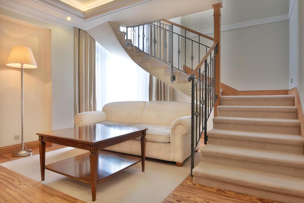 a living room with a staircase with a couch and a table at Retro Riverside Wellness Resort in Karlovy Vary