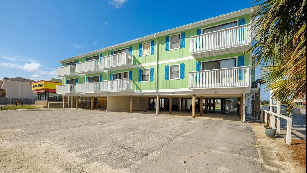 a green building with white balconies and a parking lot at The American Dream in Gulf Shores