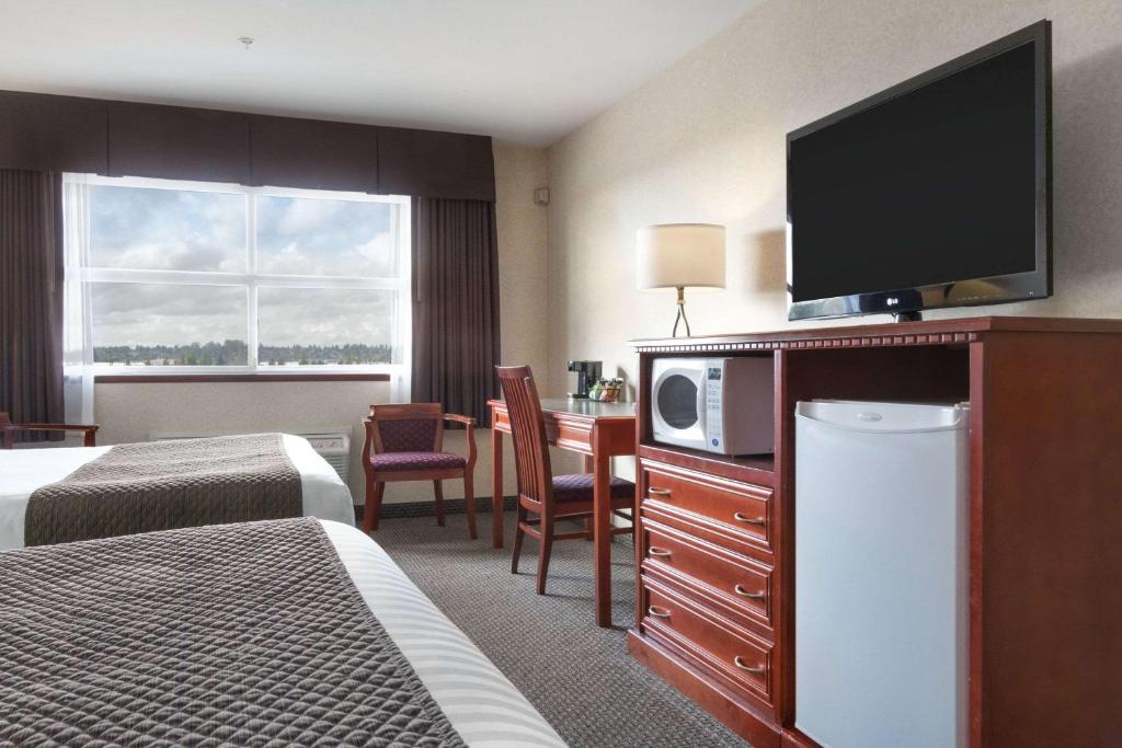 a hotel room with two beds and a television on a dresser at Days Inn & Suites by Wyndham Langley in Langley