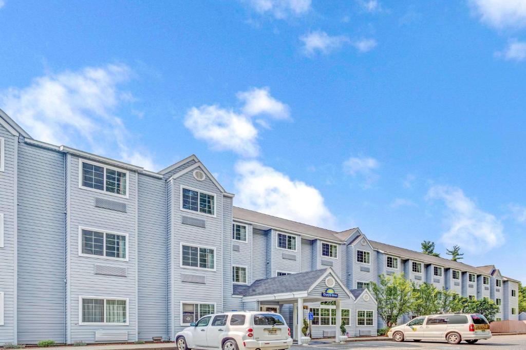 Deux voitures garées devant un grand bâtiment dans l'établissement Days Inn by Wyndham Sturbridge, à Sturbridge