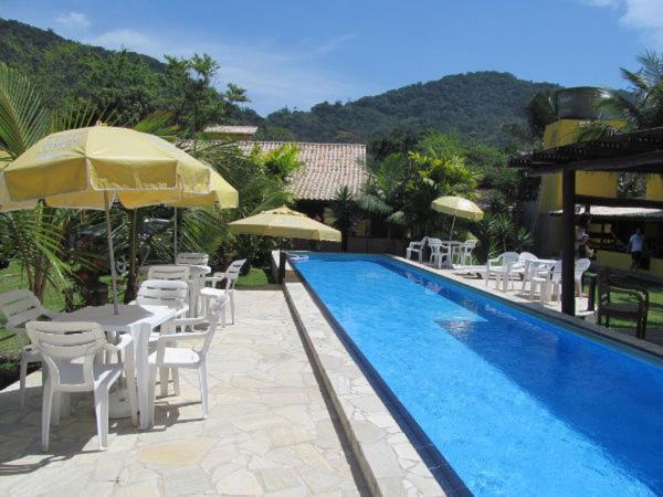una piscina con sillas blancas, mesas y sombrillas en Pousada Lugar Comum, en Boicucanga