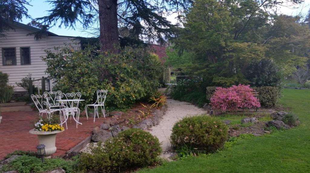 a patio with white chairs and flowers in a yard at Westering Cottage in Wandin North