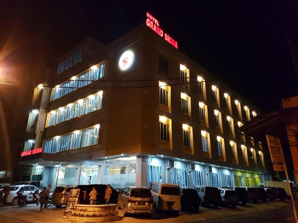 um edifício com carros estacionados em frente a ele à noite em Hotel Grand Sigma em Lahat