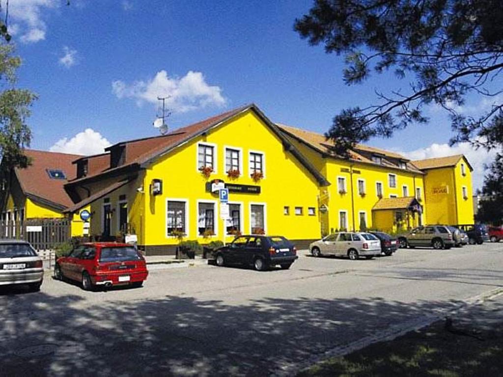Hotel ROSE Břeclav في بريكلاف: مبنى أصفر فيه سيارات متوقفة في موقف سيارات
