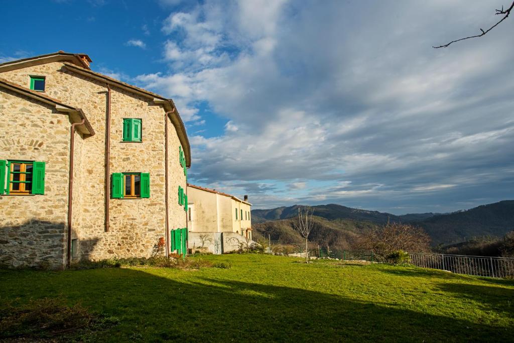 um edifício de pedra com janelas verdes num campo de relva em Villa Amamòse em Bracelli