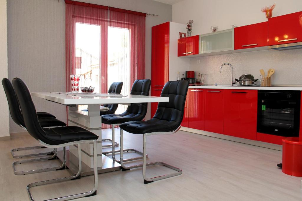 uma cozinha com armários vermelhos e uma mesa branca com cadeiras pretas em Apartmani Corleone em Bilice
