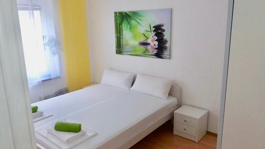 a small bedroom with a white bed with a painting on the wall at Delfin Apartments in Crikvenica