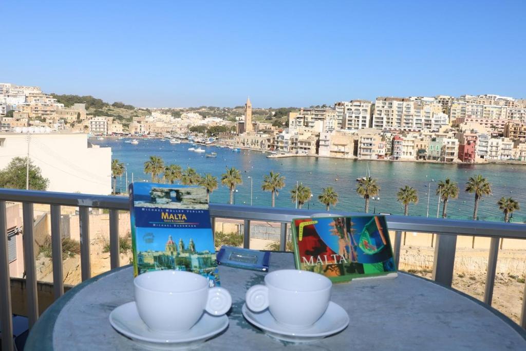 una mesa con 2 tazas y libros en el balcón en Sea front apartment, en Marsaskala