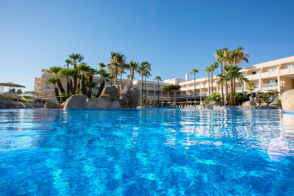a swimming pool at a resort with palm trees at Hipotels Playa La Barrosa - Adults Only in Chiclana de la Frontera