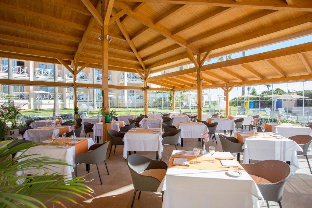a restaurant with white tables and chairs and windows at Hipotels Playa La Barrosa - Adults Only in Chiclana de la Frontera