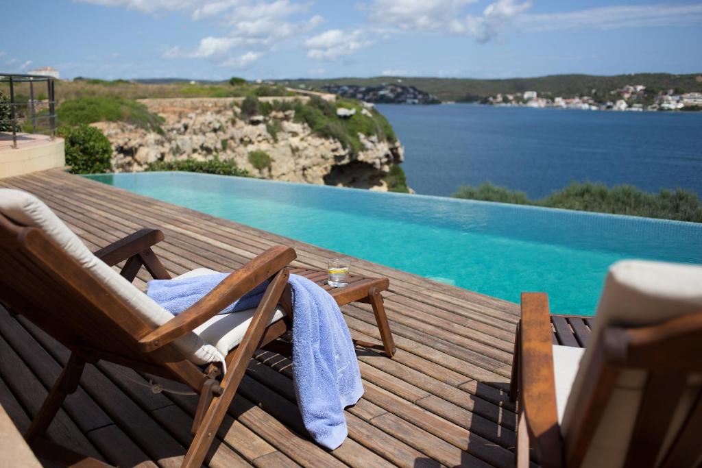 eine Holzterrasse mit 2 Stühlen und einem Pool in der Unterkunft Casa Bárbara in Es Castell