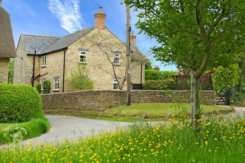 une maison en briques avec un mur en pierre et des fleurs dans l'établissement Brook Farm Cottage, à Brackley