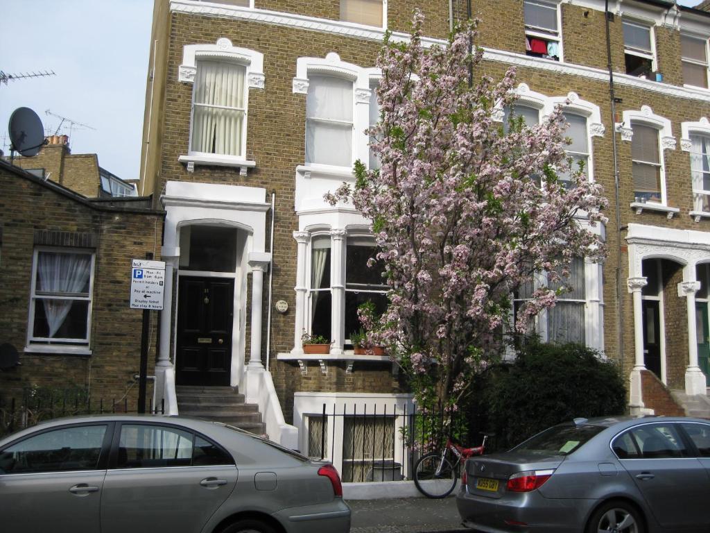 dos autos estacionados frente a una casa con un árbol florido en Olympia W14 Two-Bedroom Apartment en Londres