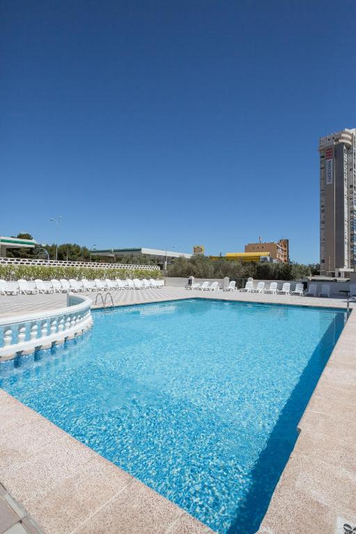 a large swimming pool with white chairs and a building at Pierre & Vacances Benidorm Levante - Adults Recommended in Benidorm