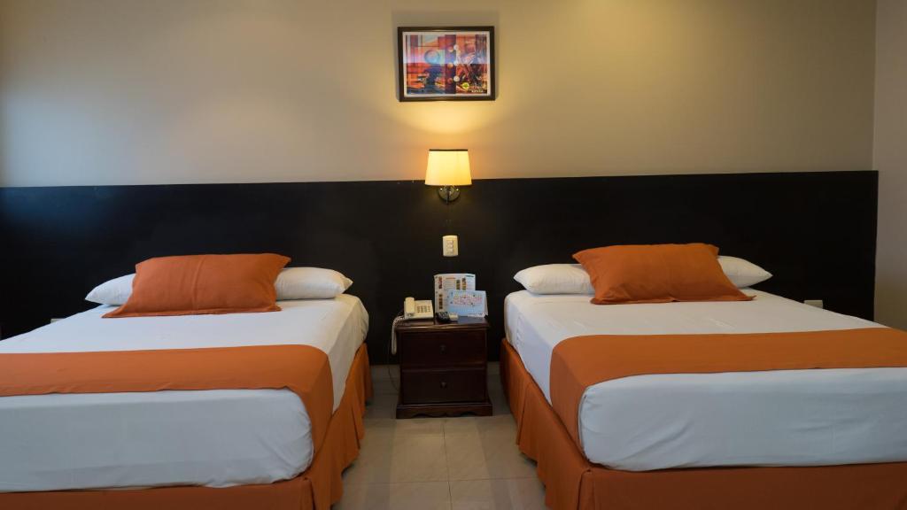 um quarto de hotel com duas camas com almofadas laranja em Hotel Los Almendros em Manta