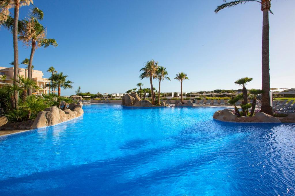 a large swimming pool with palm trees in a resort at Hipotels Playa La Barrosa - Adults Only in Chiclana de la Frontera