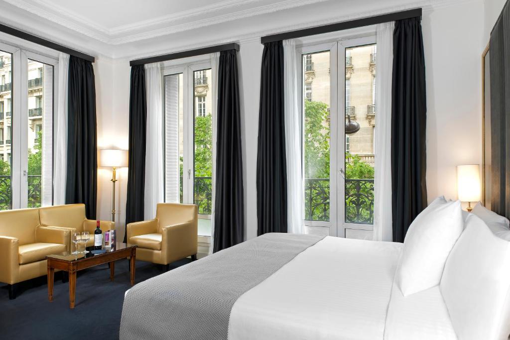 um quarto com uma cama, 2 cadeiras e janelas em Melia Paris Champs Elysées em Paris