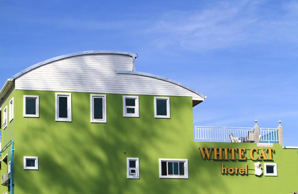 カオラックにあるホワイト キャット ホテルの白い車のホテルの看板が書かれた緑の建物