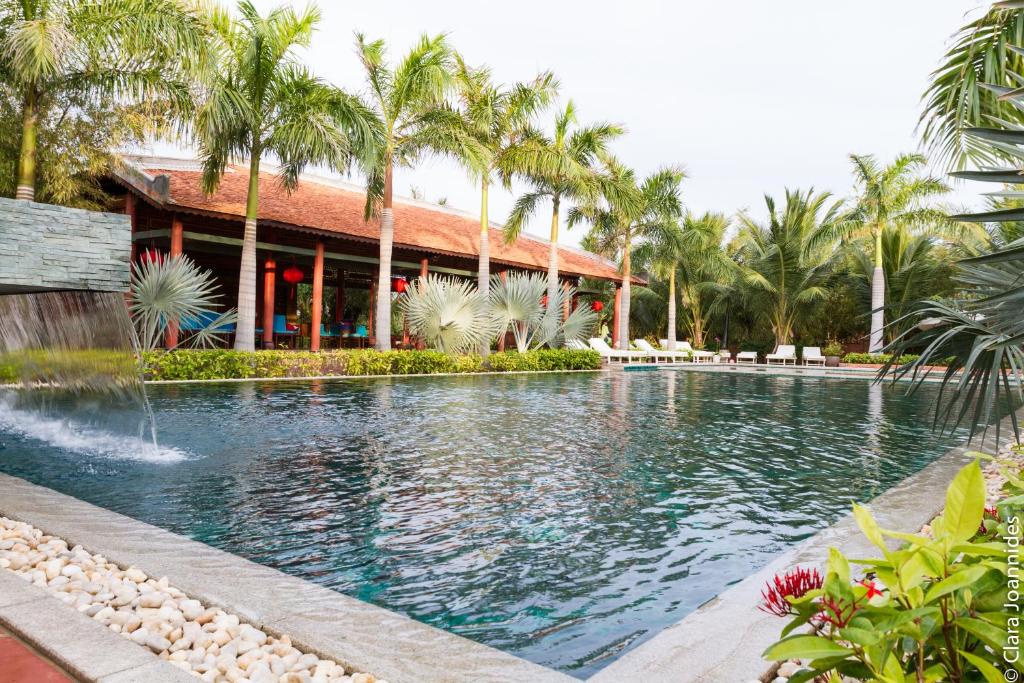 a swimming pool in front of a resort with palm trees at Full Moon Village Resort in Mui Ne