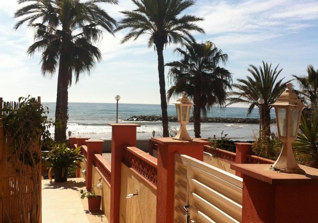 a wooden fence with palm trees and the beach at El prat beach apartment by HLCLUB Agency in Vilanova i la Geltrú
