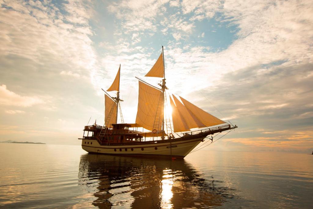 a sail boat in the water with the sun setting at Plataran Phinisi Felicia, a Luxury Private Cruise in Labuan Bajo