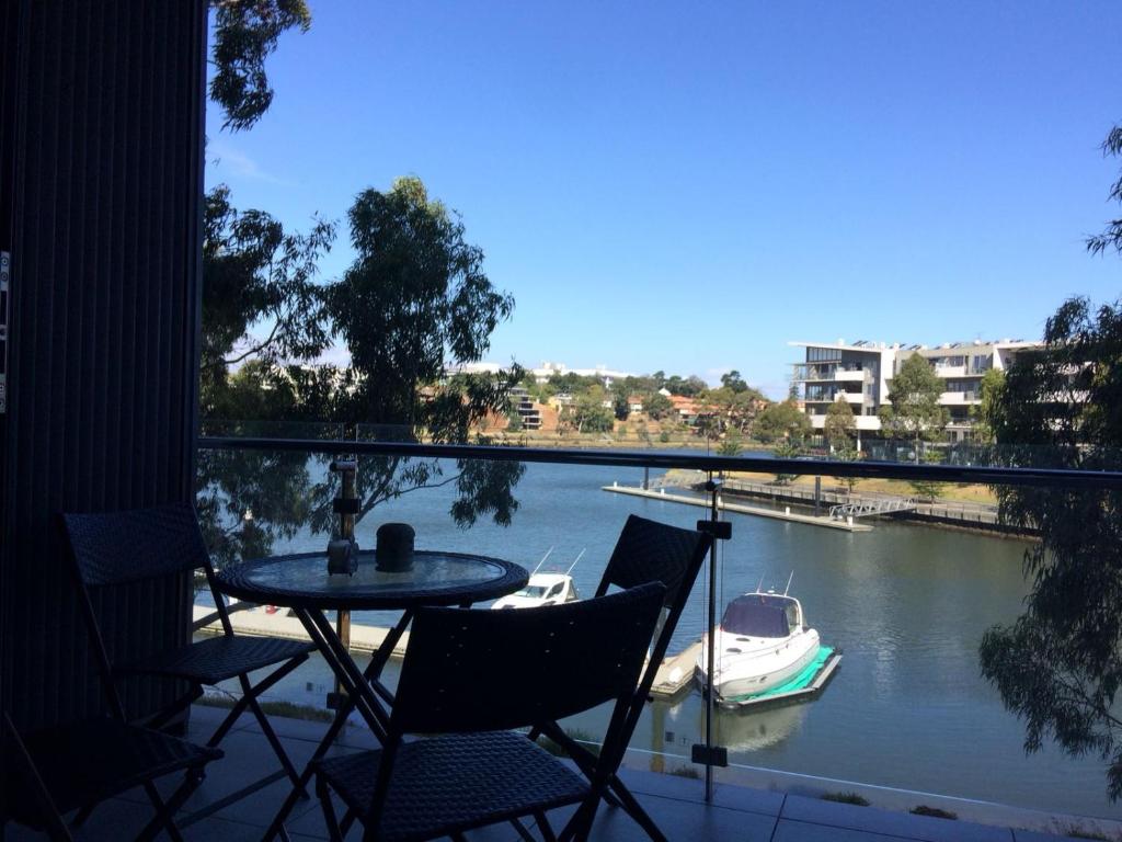 a balcony with a table and chairs and a boat in the water at Marina View Apartment on the Maribyrnong River, Melbourne in Melbourne