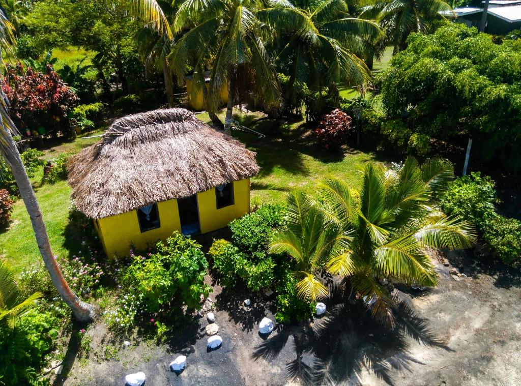 a small yellow house with a straw roof and palm trees at Yasawa Homestays in Nacula Island