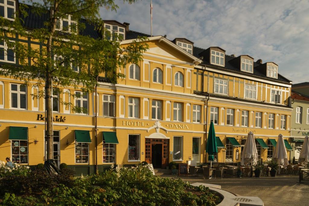 a yellow building with tables and umbrellas in front of it at Hotel Dania in Silkeborg