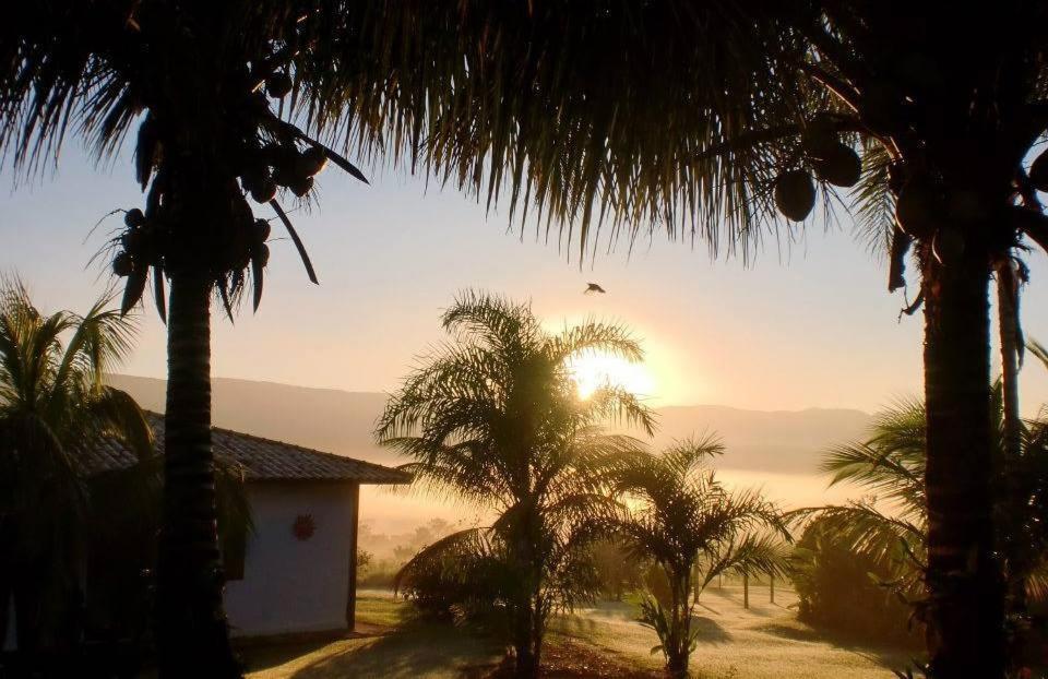 ein Haus mit Palmen und Sonnenuntergang im Hintergrund in der Unterkunft Pousada da Lua in Delfinópolis